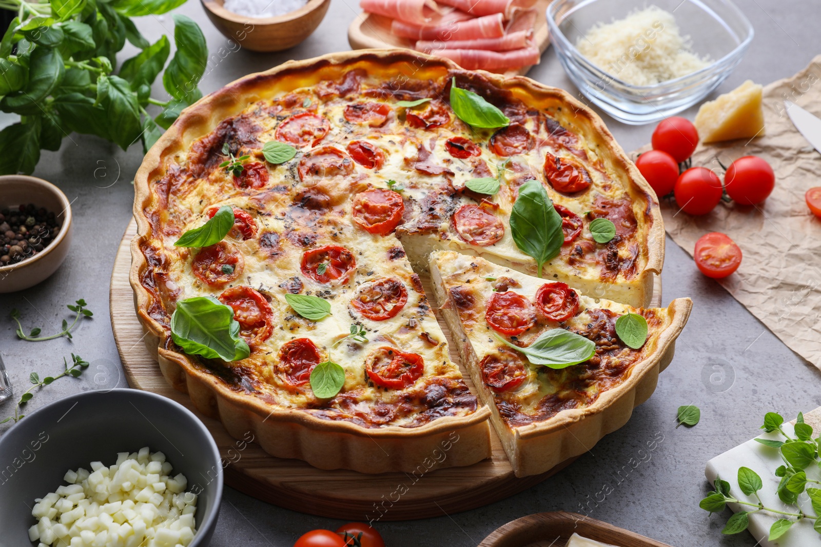 Photo of Cut delicious homemade quiche with prosciutto and ingredients on light grey table