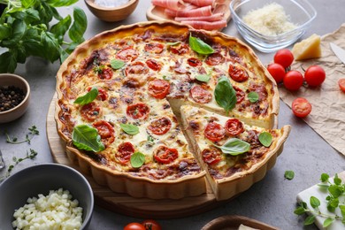 Photo of Cut delicious homemade quiche with prosciutto and ingredients on light grey table