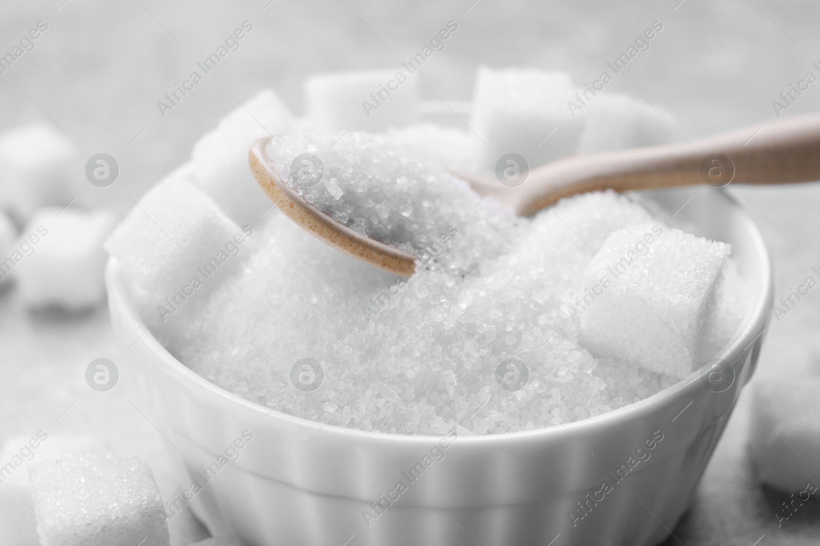 Photo of Different types of white sugar in bowl on grey table, closeup