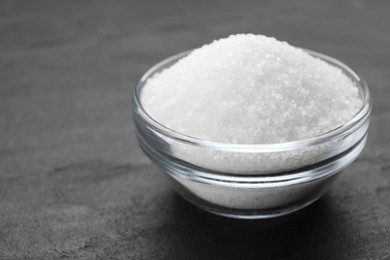 White granulated sugar in bowl on black table, closeup. Space for text