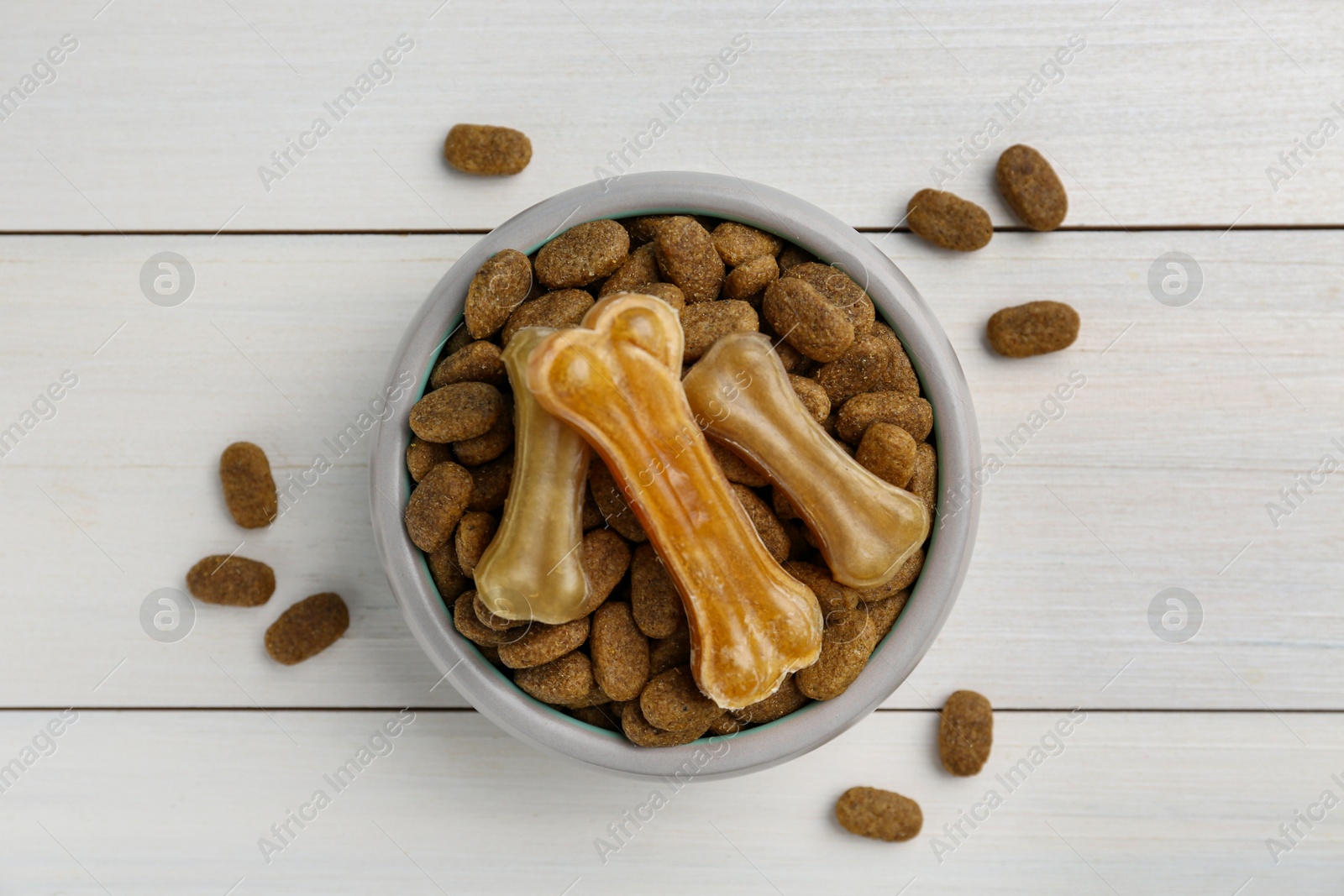 Photo of Dry dog food and treats (chew bones) on white wooden floor, flat lay