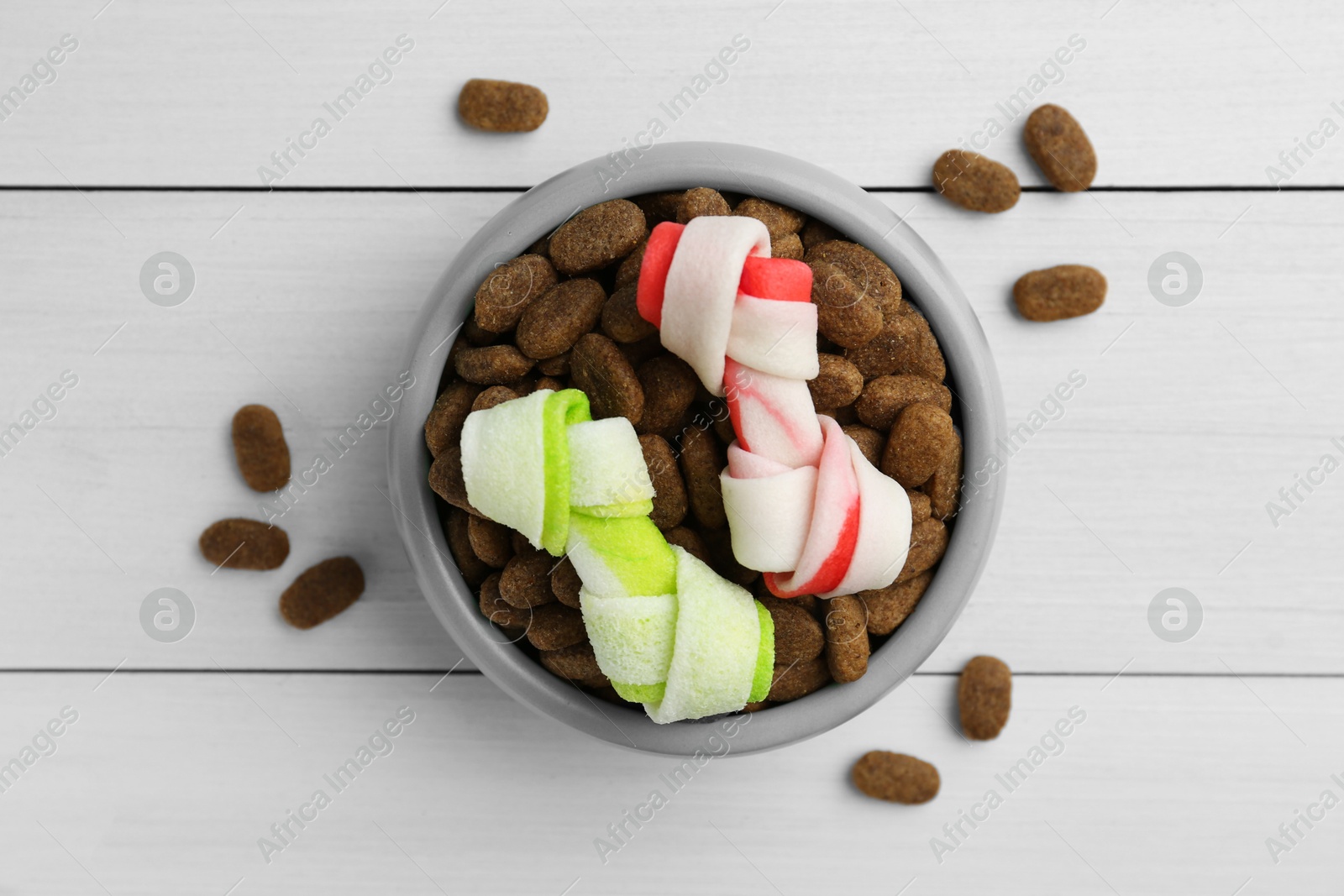 Photo of Dry dog food and treats (knotted chew bones) on white wooden floor, flat lay