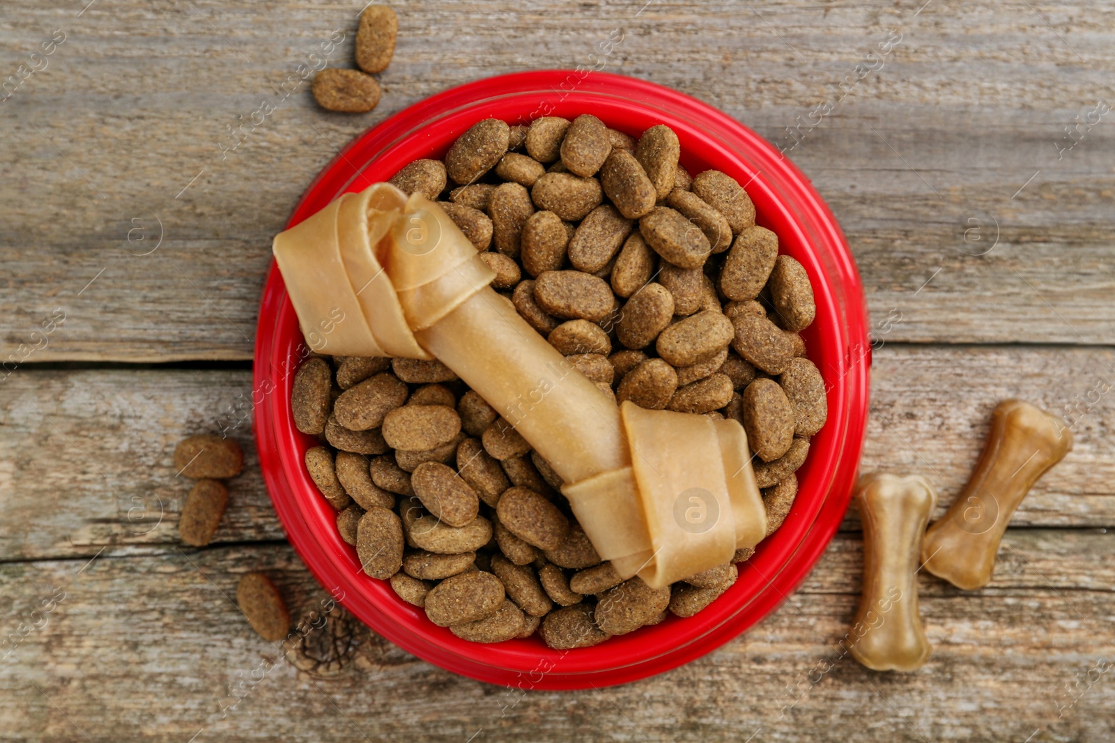 Photo of Dry dog food and treats (chew bones) on wooden floor, flat lay