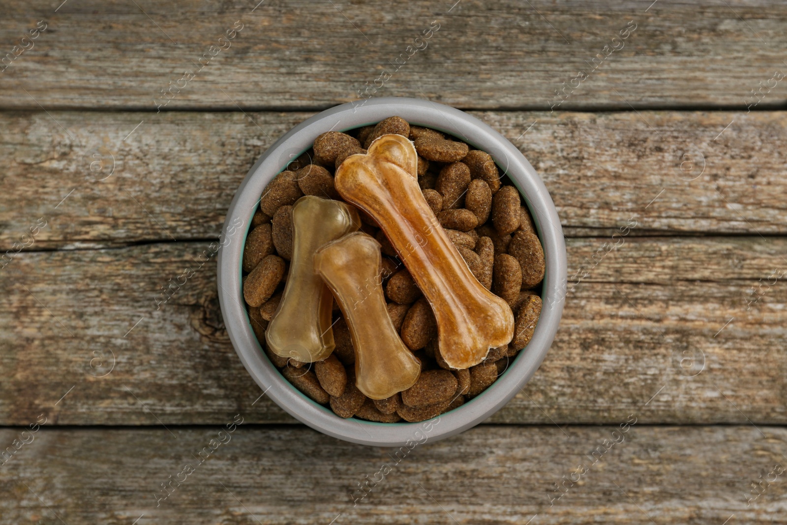 Photo of Dry dog food and treats (chew bones) on wooden floor, top view