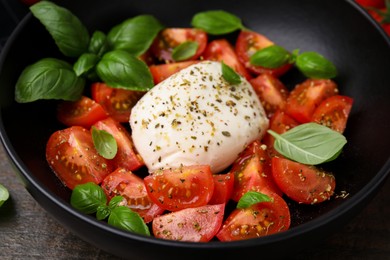 Photo of Tasty salad Caprese with mozarella, tomatoes and basil in black bowl, closeup