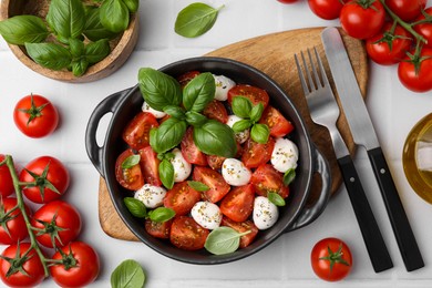 Photo of Tasty salad Caprese with mozarella balls, tomatoes and basil served on white tiled table, flat lay