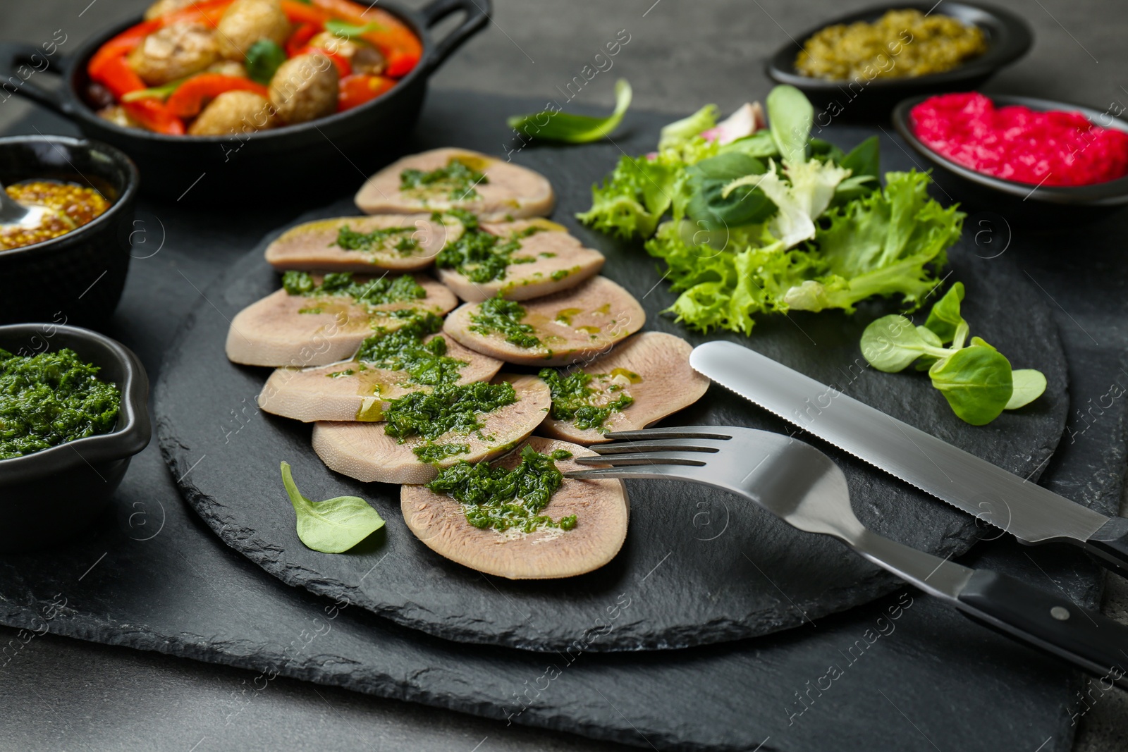 Photo of Tasty beef tongue pieces and ingredients served on grey table, closeup