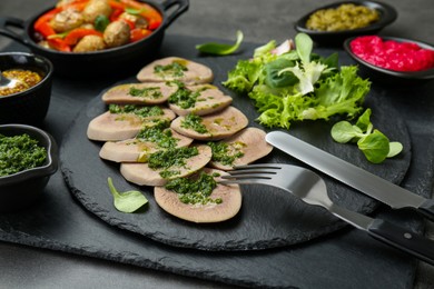 Photo of Tasty beef tongue pieces and ingredients served on grey table, closeup