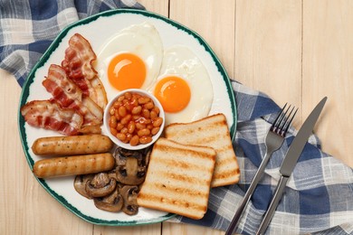 Plate with fried eggs, sausages, mushrooms, beans, bacon and toasts on wooden table, flat lay. Traditional English breakfast