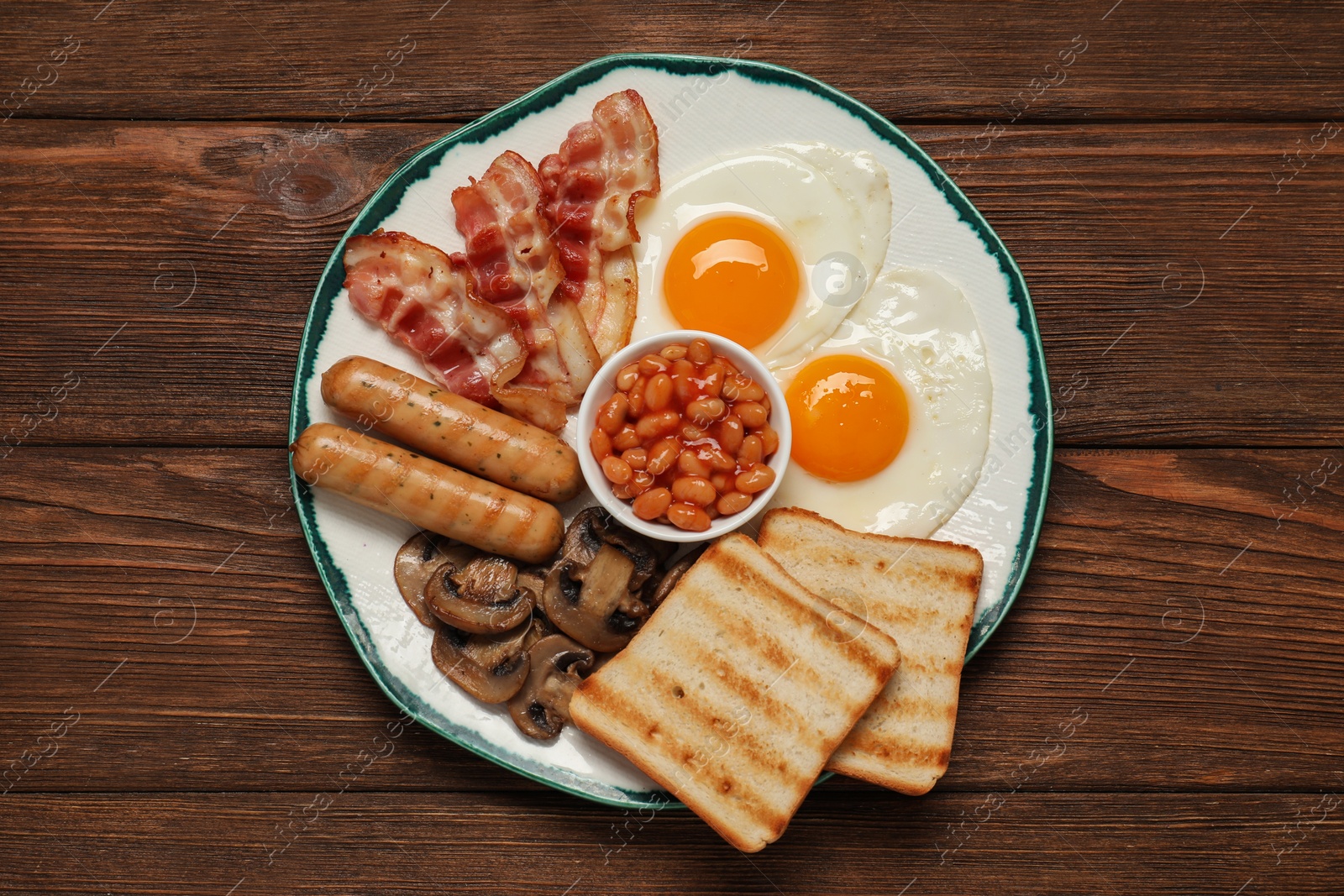 Photo of Plate with fried eggs, sausages, mushrooms, beans, bacon and toasts on wooden table, top view. Traditional English breakfast