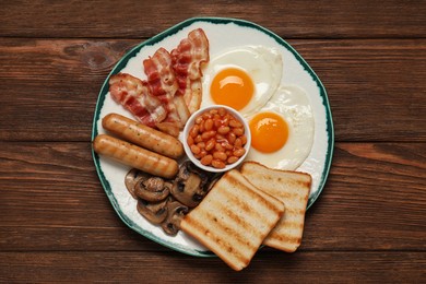 Plate with fried eggs, sausages, mushrooms, beans, bacon and toasts on wooden table, top view. Traditional English breakfast