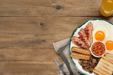 Plate of fried eggs, sausages, mushrooms, beans, bacon and toasts on wooden table, flat lay with space for text. Traditional English breakfast