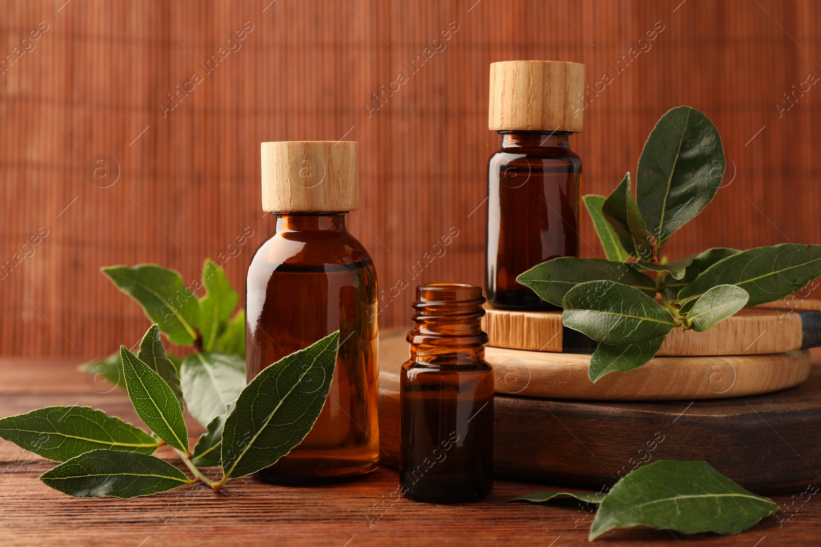 Photo of Bottles of bay essential oil and fresh leaves on wooden table