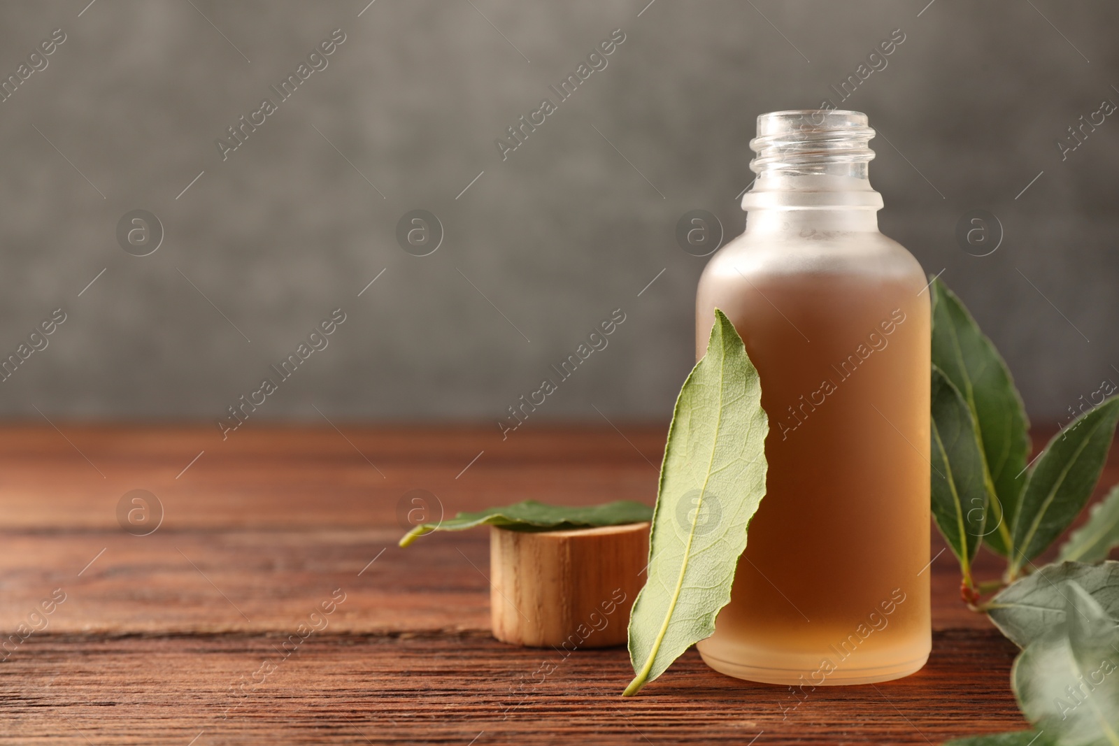 Photo of Bottle of bay essential oil and fresh leaves on wooden table, closeup. Space for text