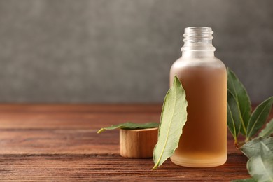 Photo of Bottle of bay essential oil and fresh leaves on wooden table, closeup. Space for text