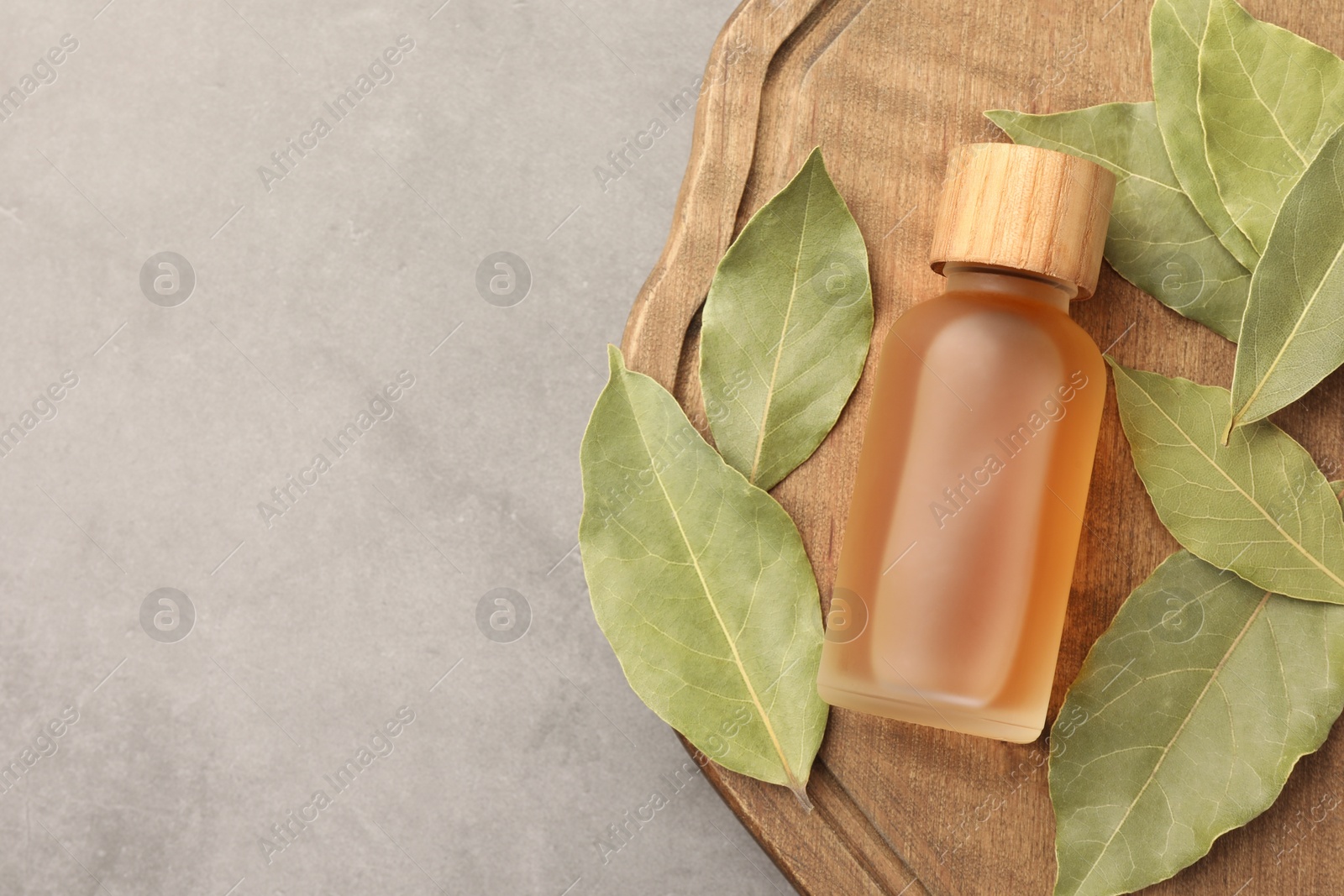 Photo of Bottle of bay essential oil and dried leaves on light grey table, top view. Space for text