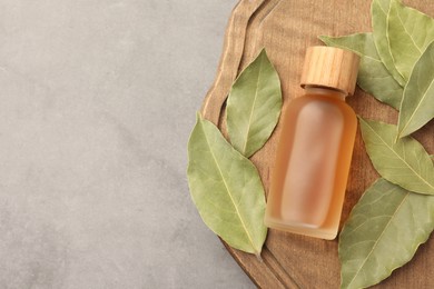 Bottle of bay essential oil and dried leaves on light grey table, top view. Space for text