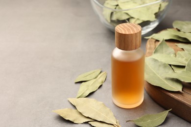 Photo of Bottle of bay essential oil and dried leaves on light grey table. Space for text