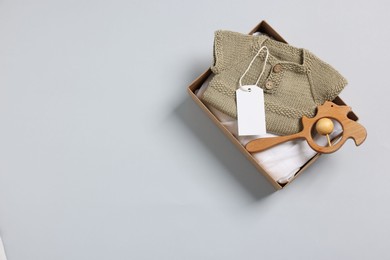 Photo of Different baby accessories, clothes and blank card in box on light grey background, top view. Space for text