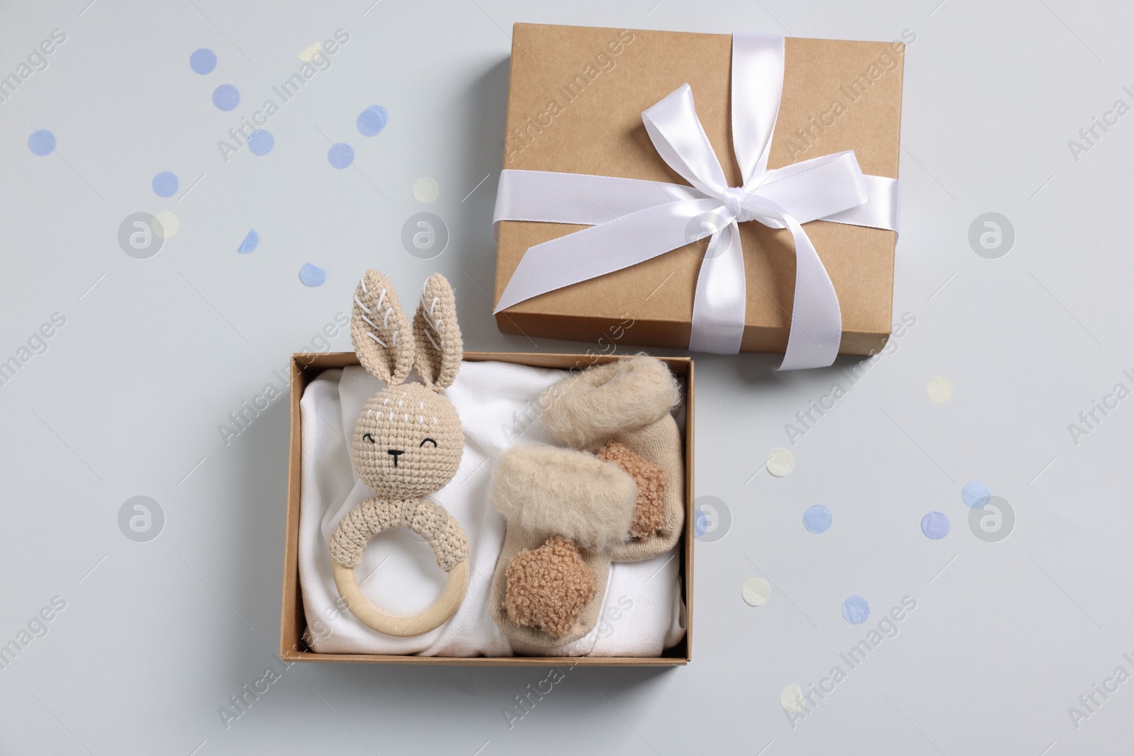 Photo of Different baby accessories in box and confetti on light grey background, flat lay