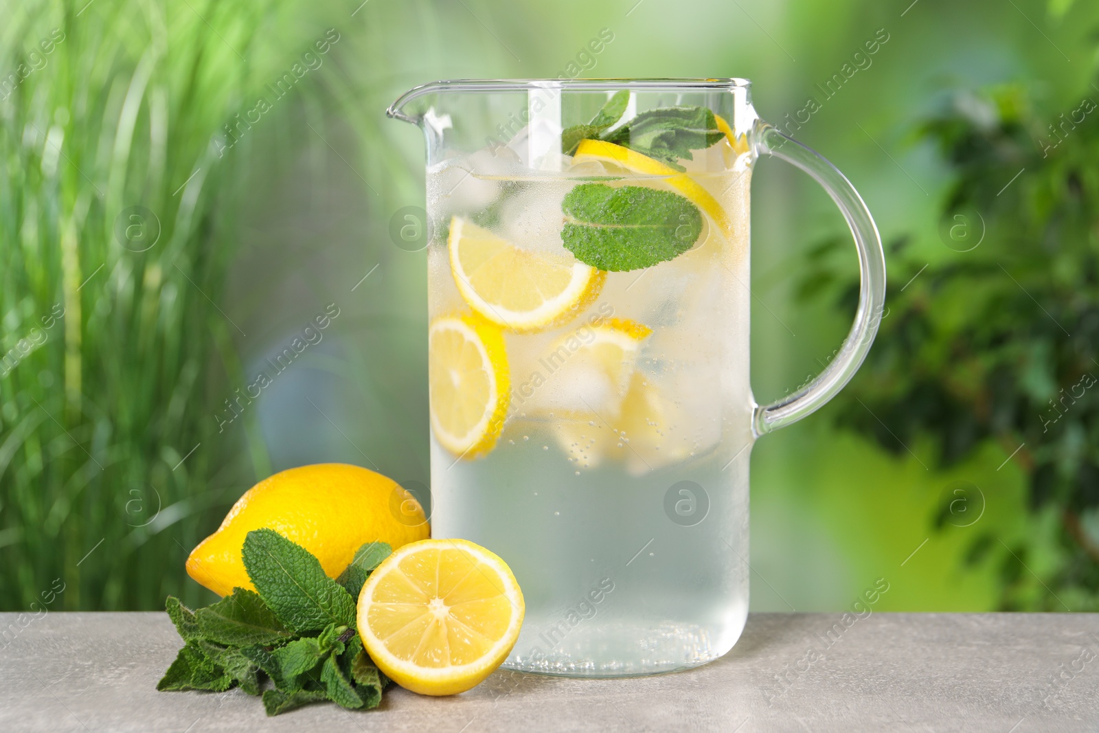 Photo of Freshly made lemonade with mint in jug on grey table outdoors