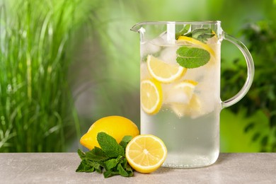 Photo of Freshly made lemonade with mint in jug on grey table outdoors, space for text