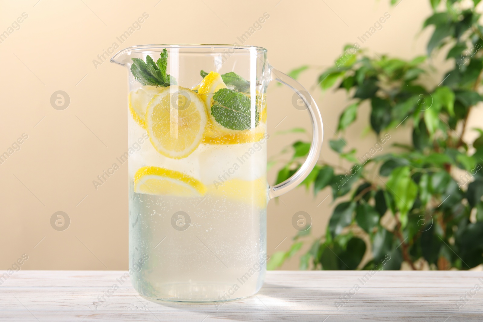 Photo of Freshly made lemonade with mint in jug on white wooden table against beige background