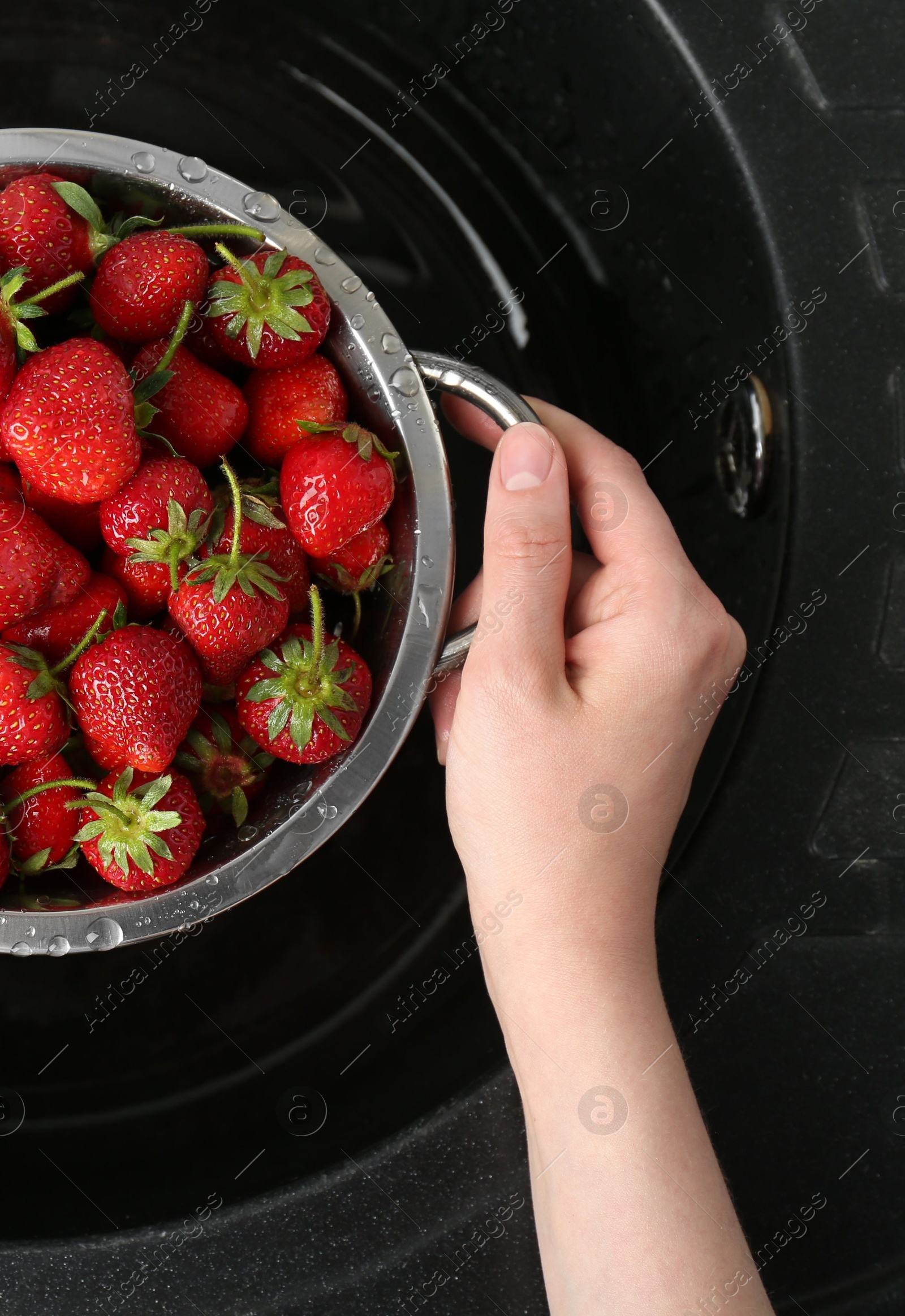 Photo of Woman with metal colander of fresh wet strawberries above sink, top view