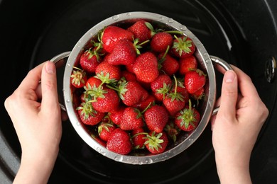 Photo of Woman with metal colander of fresh wet strawberries above sink, top view