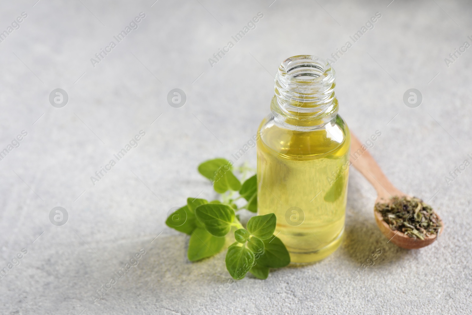 Photo of Essential oil in bottle, oregano leaves and spoon with dry herb on light grey textured table, closeup. Space for text