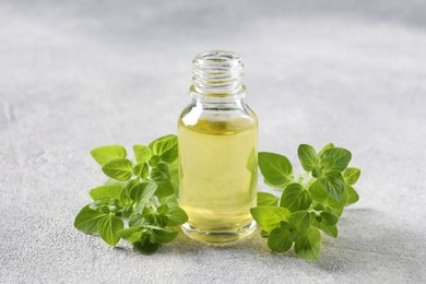 Essential oil in bottle and oregano leaves on light grey textured table, closeup