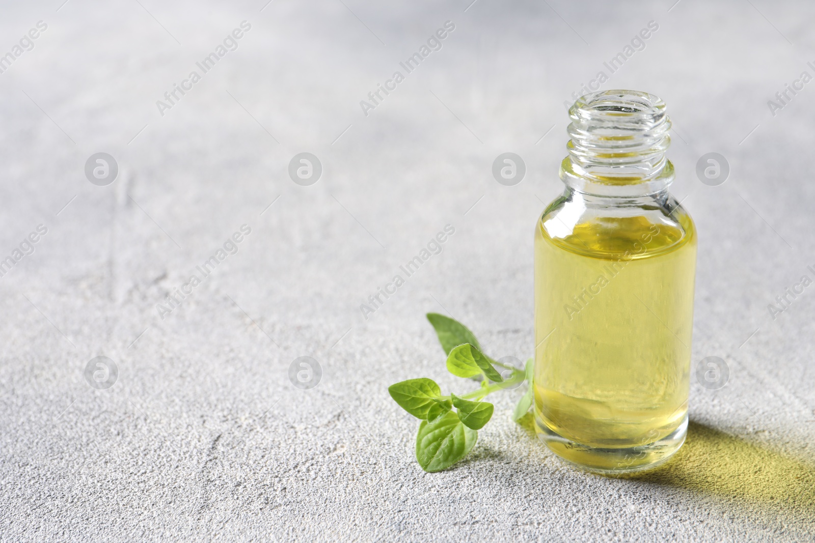 Photo of Essential oil in bottle and oregano leaves on light grey textured table, closeup. Space for text