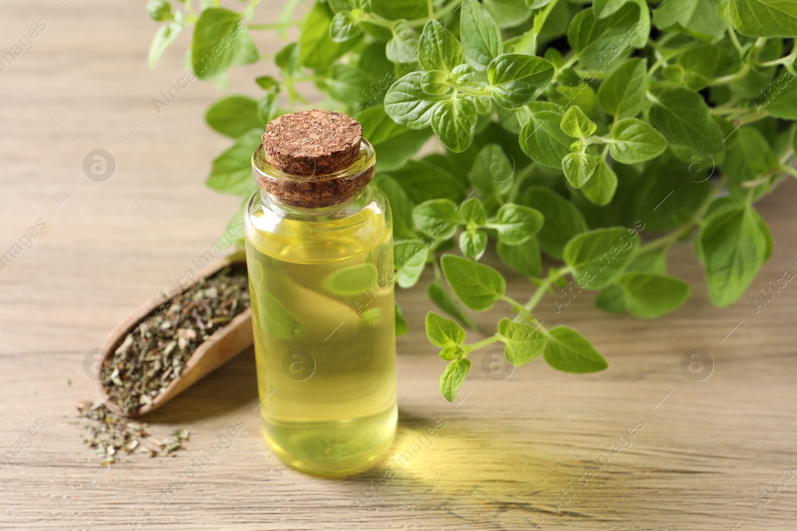 Photo of Essential oil in bottle, scoop with dry herb and oregano leaves on wooden table, closeup