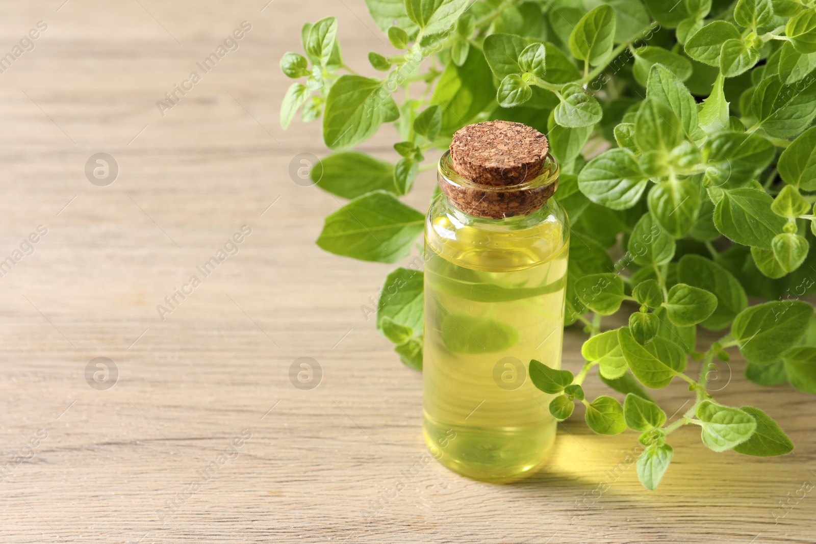 Photo of Essential oil in bottle and oregano leaves on wooden table, closeup. Space for text