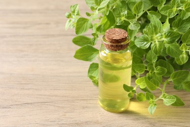 Essential oil in bottle and oregano leaves on wooden table, closeup. Space for text