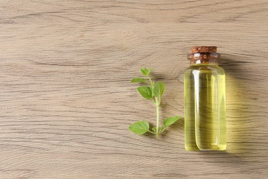 Essential oil in bottle and oregano twig on wooden table, top view. Space for text