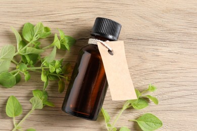 Essential oil in bottle with empty tag and oregano leaves on wooden table, flat lay