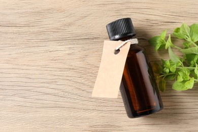 Photo of Essential oil in bottle with empty tag and oregano leaves on wooden table, flat lay. Space for text