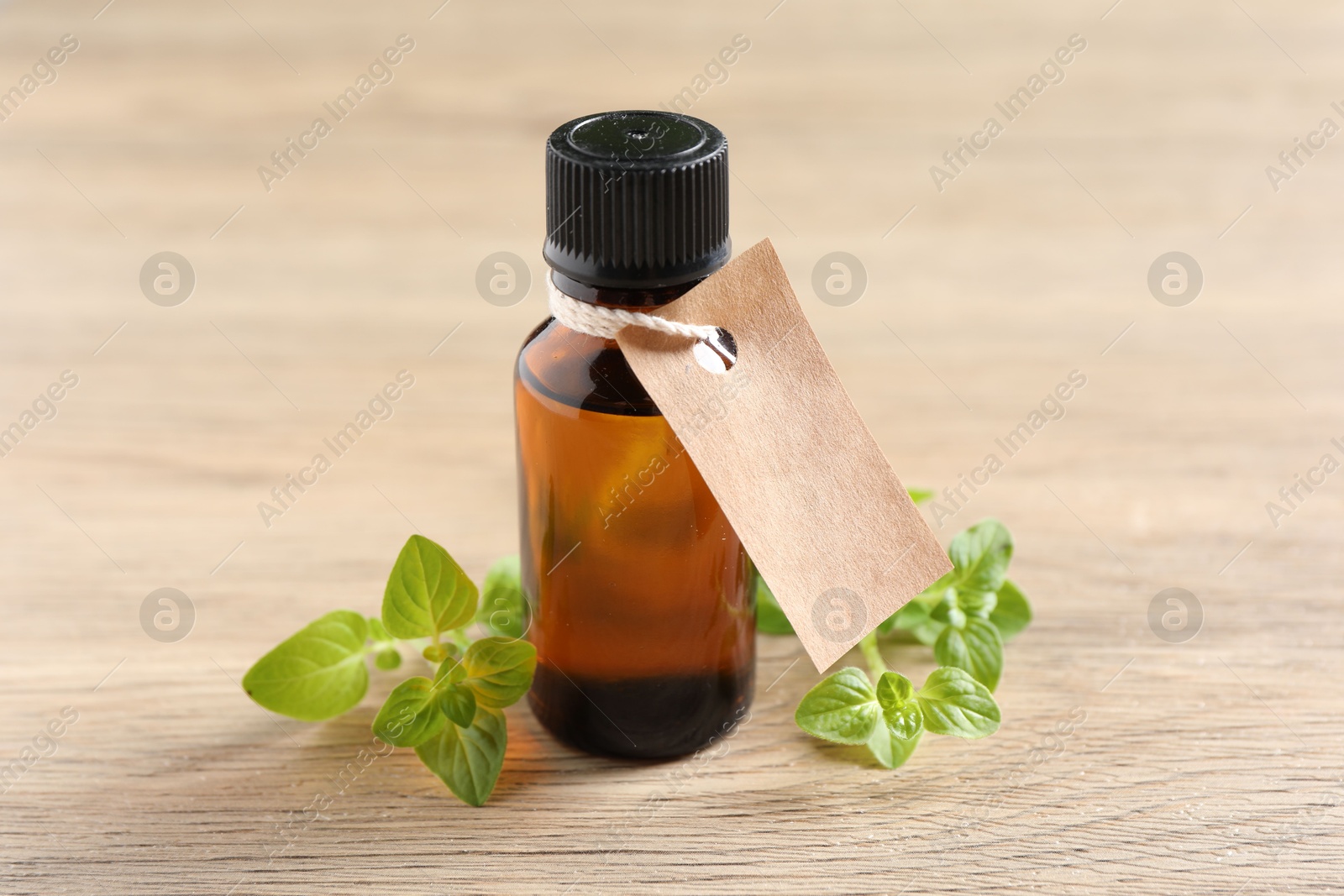 Photo of Essential oil in bottle with empty tag and oregano leaves on wooden table, closeup