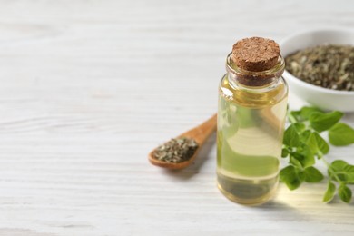 Essential oil in bottle, dry herb and oregano leaves on white wooden table, closeup. Space for text