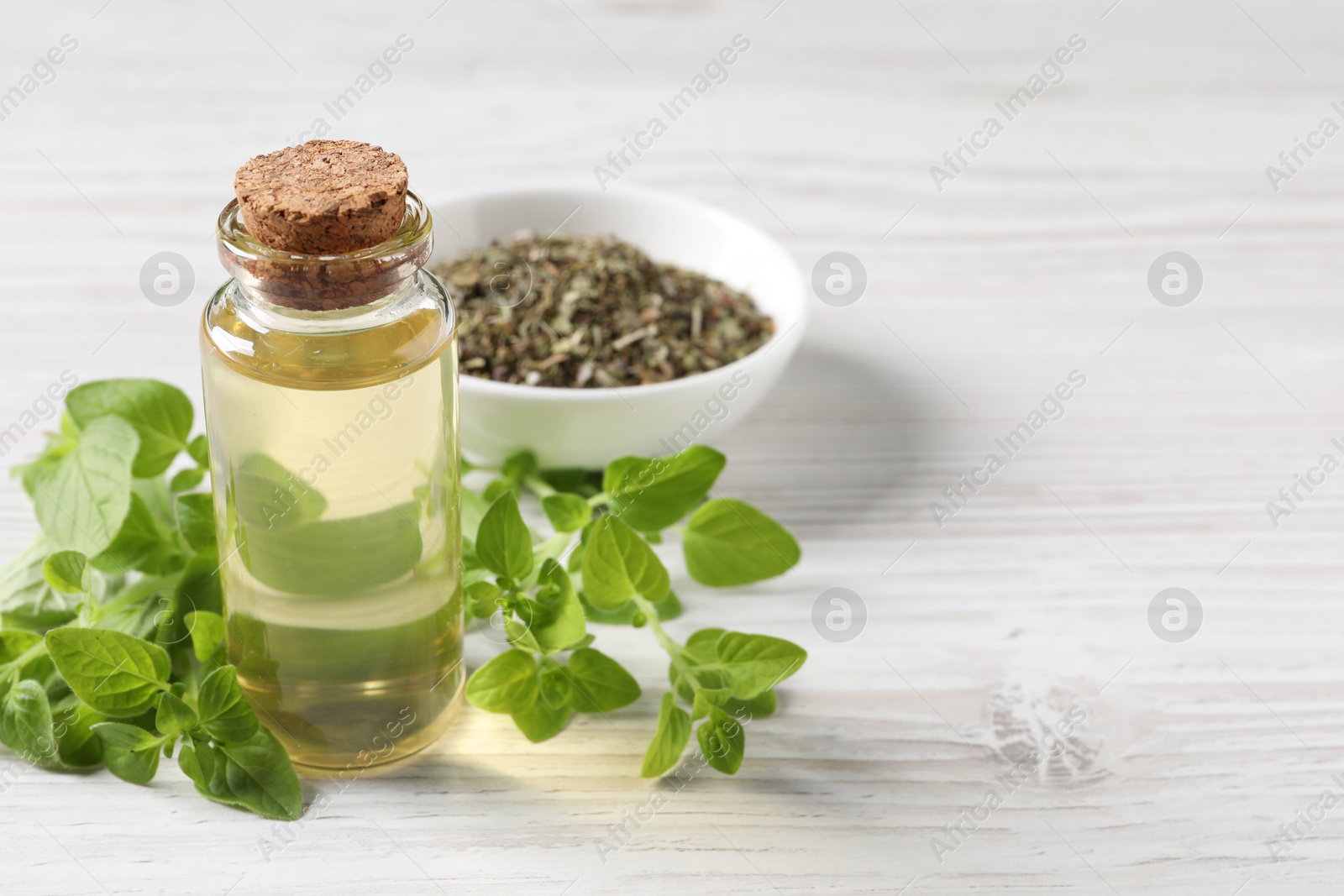 Photo of Essential oil in bottle, dry herb and oregano leaves on white wooden table, closeup. Space for text