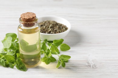 Essential oil in bottle, dry herb and oregano leaves on white wooden table, closeup. Space for text