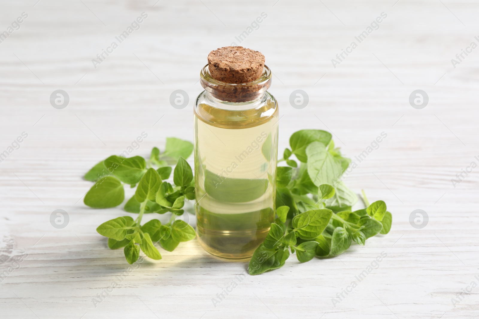 Photo of Essential oil in bottle and oregano leaves on white wooden table, closeup