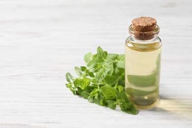 Essential oil in bottle and oregano leaves on white wooden table, closeup. Space for text