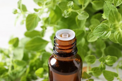 Essential oil in bottle and oregano leaves on white background, closeup