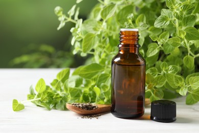 Photo of Essential oil in bottle, dry herbs and oregano leaves on white wooden table against blurred green background, closeup