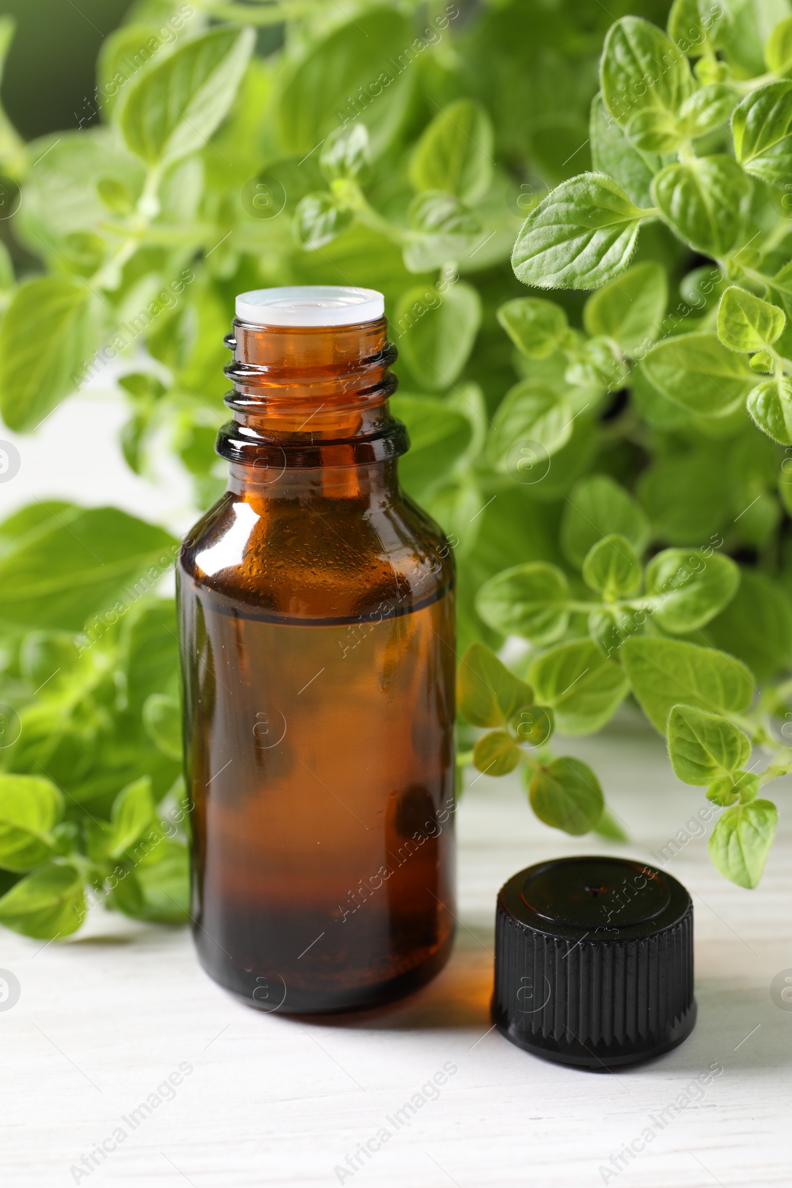 Photo of Essential oil in bottle and oregano leaves on white wooden table, closeup