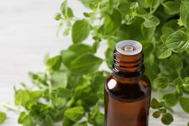 Essential oil in bottle and oregano leaves on white background, closeup. Space for text