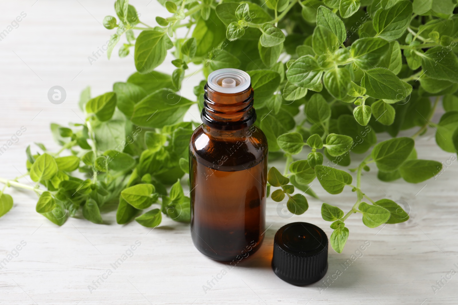 Photo of Essential oil in bottle and oregano leaves on white wooden table, closeup