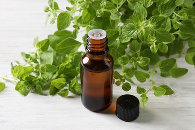 Essential oil in bottle and oregano leaves on white wooden table, closeup